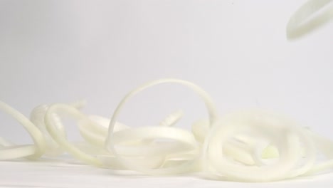 círculos de cebolla blanca perfectamente redondos que caen y rebotan en la parte superior de la mesa blanca en cámara lenta