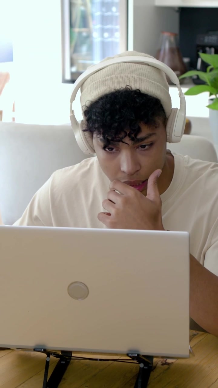 Vertical video: Audio playing man in beanie headphones taking notes studying home notebook laptop