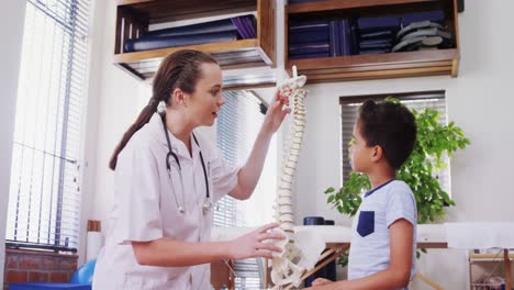 fisioterapeuta explicando el modelo de la columna vertebral al niño paciente 4k