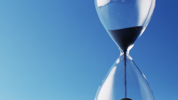 Video of close up of hourglass with black sand pouring with copy space on blue background