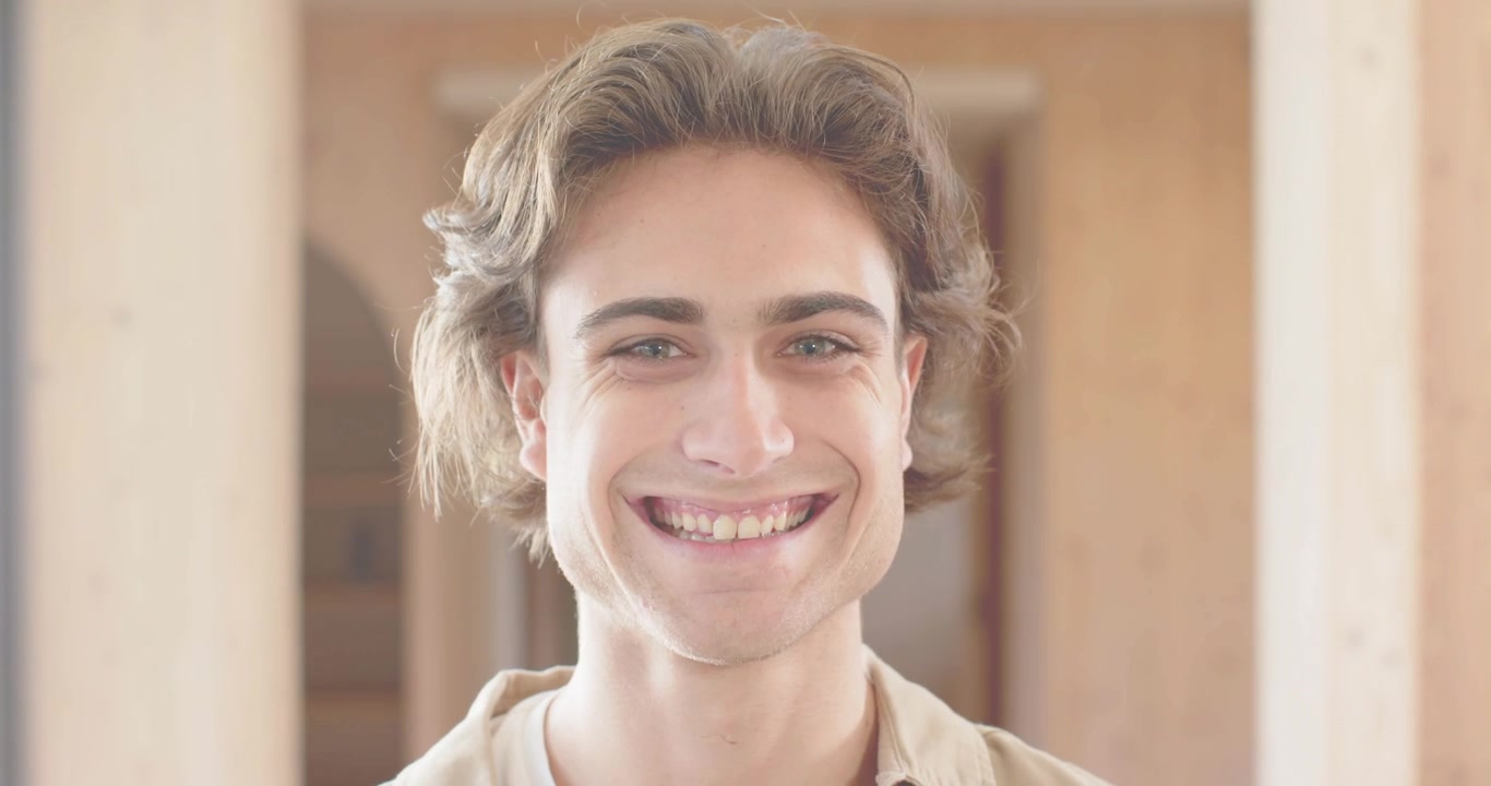 Homem em pé em um salão durante uma demonstração de tecnologia, focado enquanto uma luz rosa desliza pelo seu rosto, revelando um sorriso.