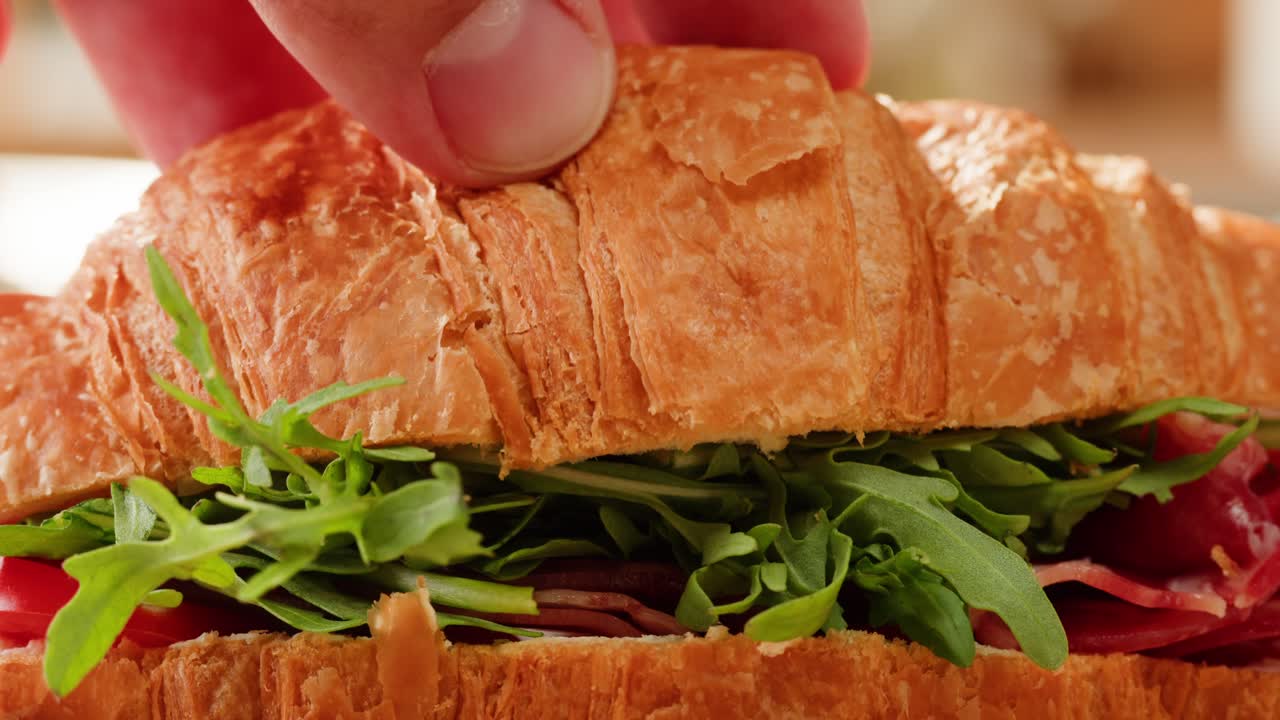 Hand placing a croissant sandwich