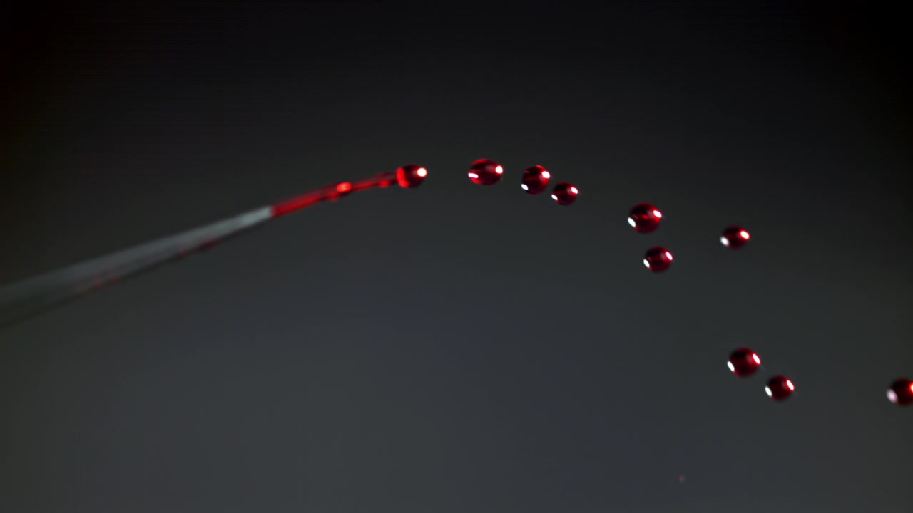 Gocce di liquido rosso che cadono al rallentatore da una pipetta