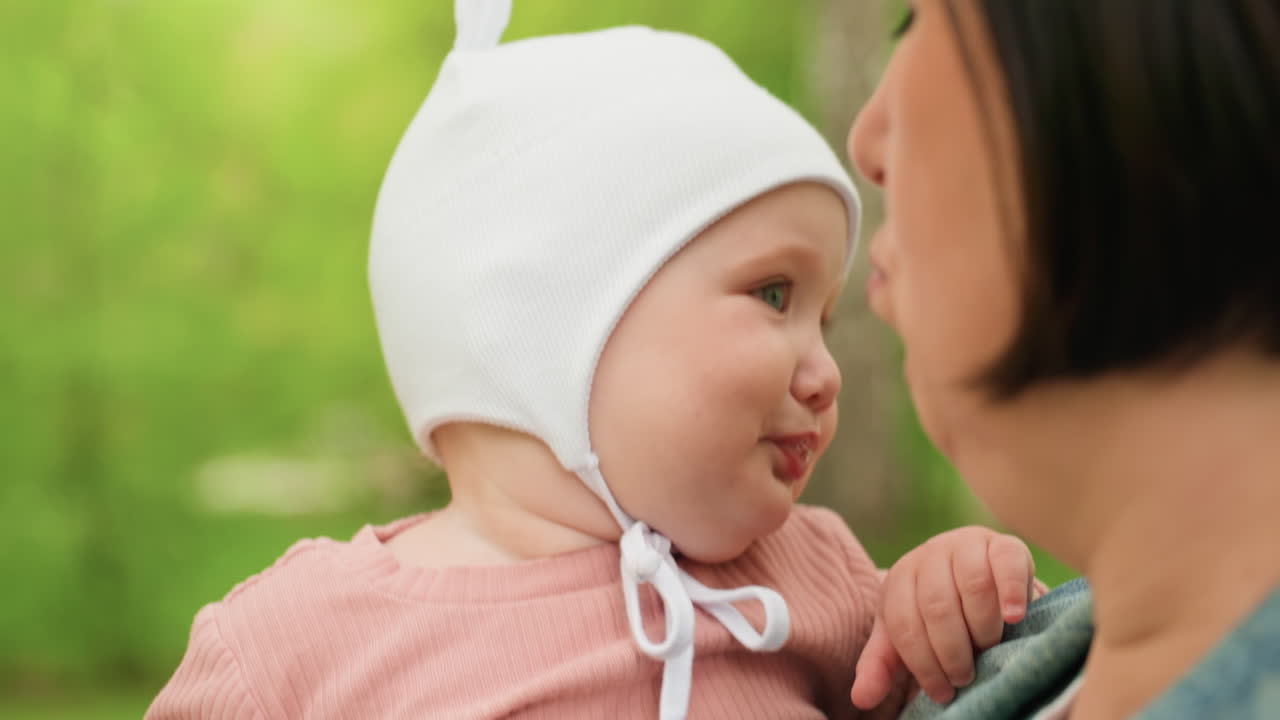 Infant Smiles During Playful Encounter, Young Child Exhibits Cheerful Reactions To Park Scene With Woman, Infant In White Hat Shows Delight And Engagement Through Expressive Faces And Smiles