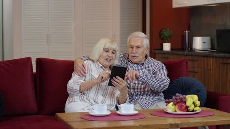 Senior-pensioner-couple-with-digital-tablet-pc-computer-at-home.-Resting-on-sofa-in-cozy-living-room