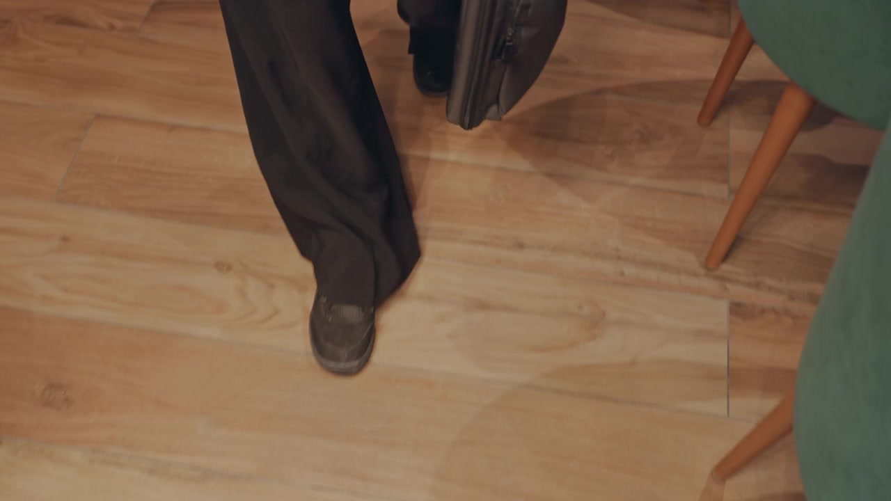 Running through room. Man moves quickly toward meeting. Individual hurriedly approaches scheduled meeting location. Person swiftly navigates wooden floor as they head to business meeting