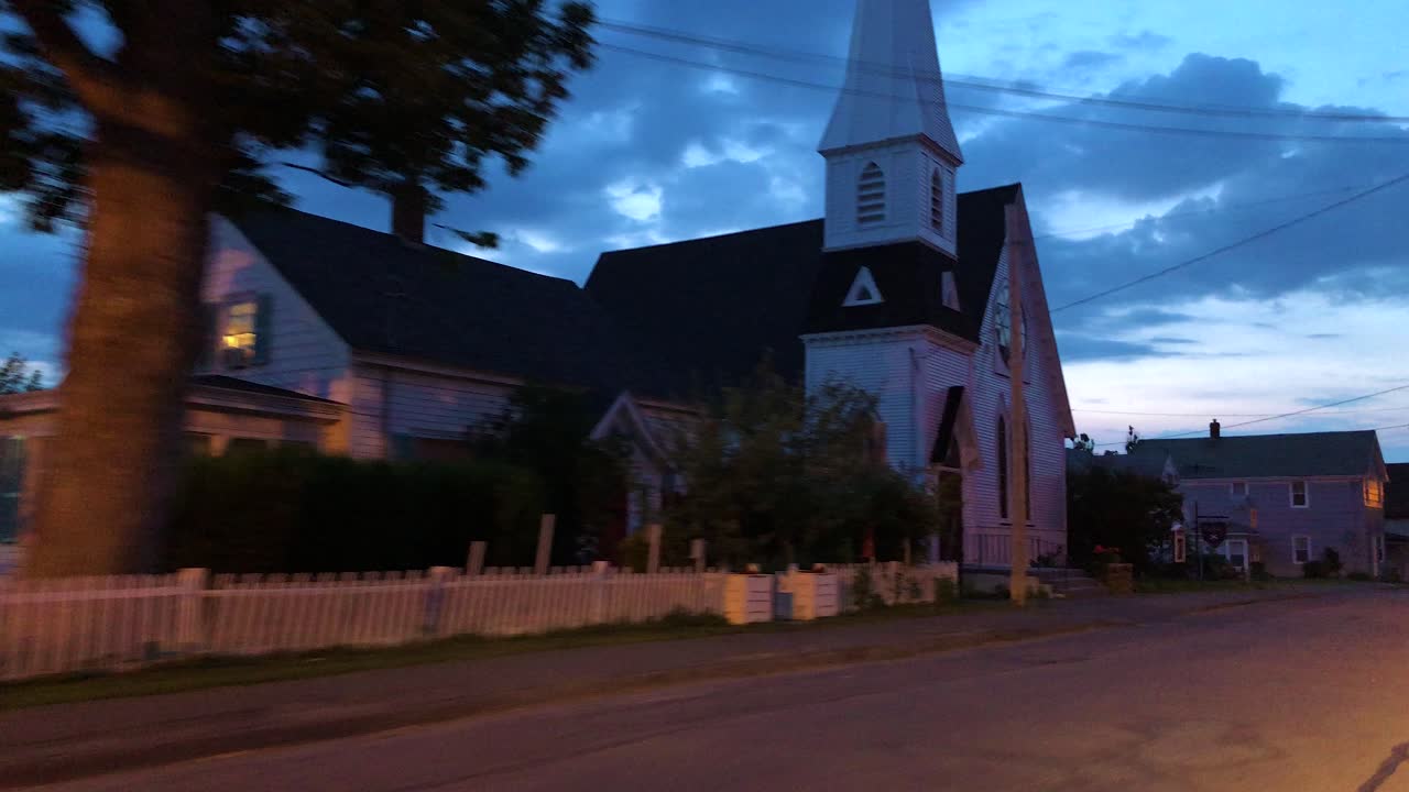 View from the drivers window driving down the street at dusk passing by a rural church