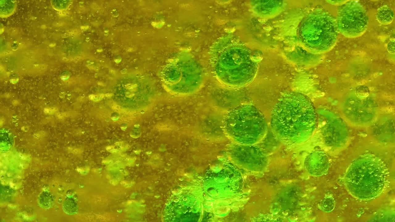 Close-up view of green bubbles rising in a yellow liquid, showcasing dynamic movement and interaction.