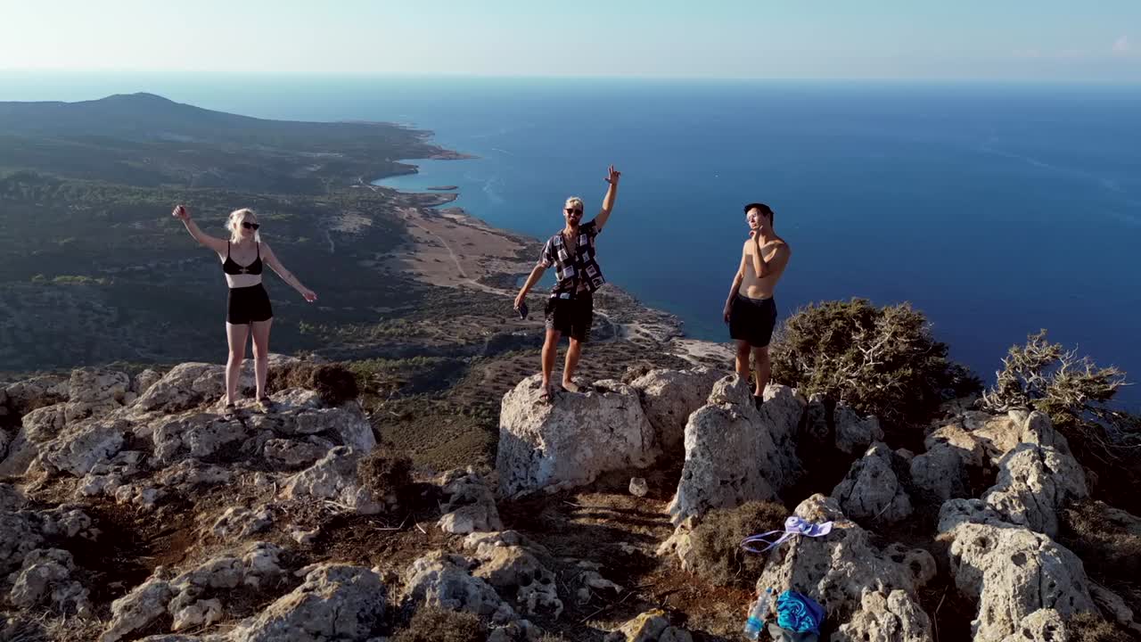 A dramatic drone shot captures three friends on rocky terrain, swiftly ascending to reveal the expansive landscape, making the subjects gradually appear smaller.