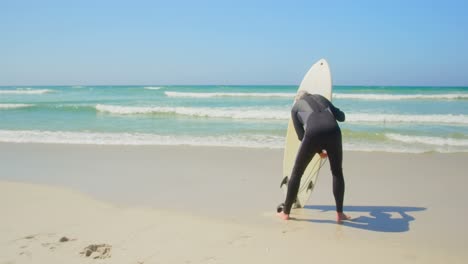 rear view of active senior caucasian male surfer standing with surfboard on the beach 4k