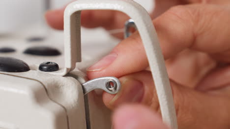 close up of female hand fixing yarn thread on thread guide of sewing machine, demonstrating precise technique, mechanical detail, gentle tension, and careful handling in minimal workspace