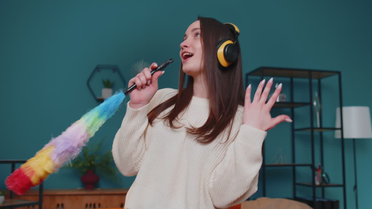 춤을 추는 젊은 여성은 가구를 혼자 고 집에 있는 방에서 다채로운 먼지를 사용하여 위생을 돌보고 있습니다.