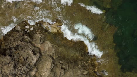 Aerial-rising-view-looking-down-over-Mallorca-ocean-waves-crashing-against-rocky-coastal-shoreline