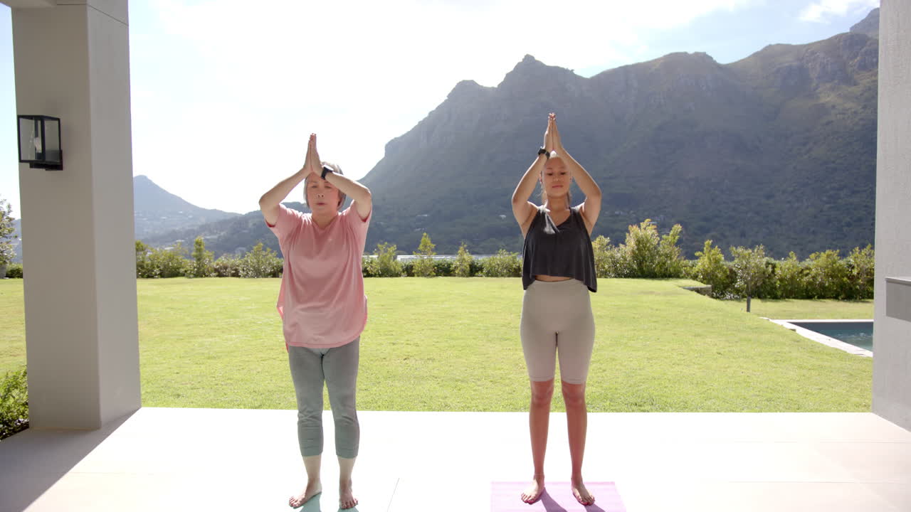 Practicing yoga, two women standing on yoga mats outdoors in mountain setting