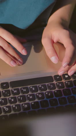 primer plano de una mujer sentada al aire libre por la noche, escribiendo en una computadora portátil con las manos iluminadas por el brillo de la pantalla, los vaqueros denim se reflejan sutilmente en la superficie de la computadora portatil, con una bolsa roja cerca
