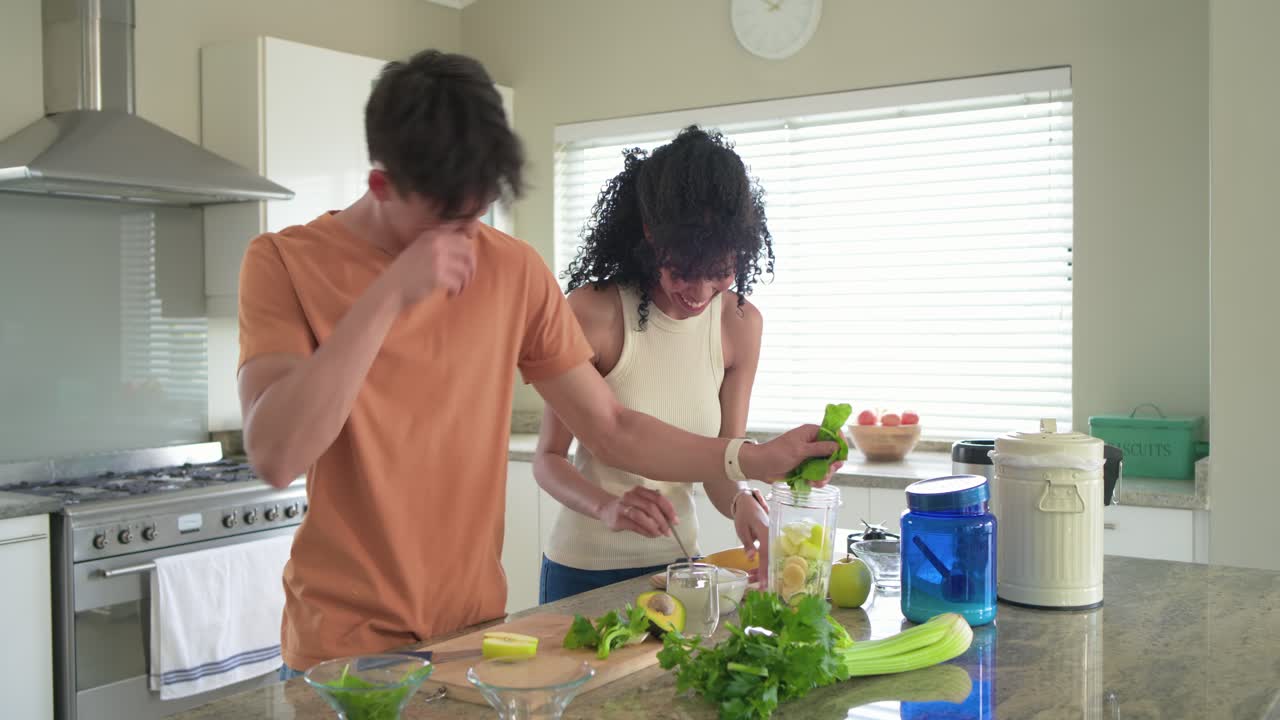 Homem asiático e mulher afro-americana preparando um smoothie no liquidificador, adicionando abacate e iogurte.