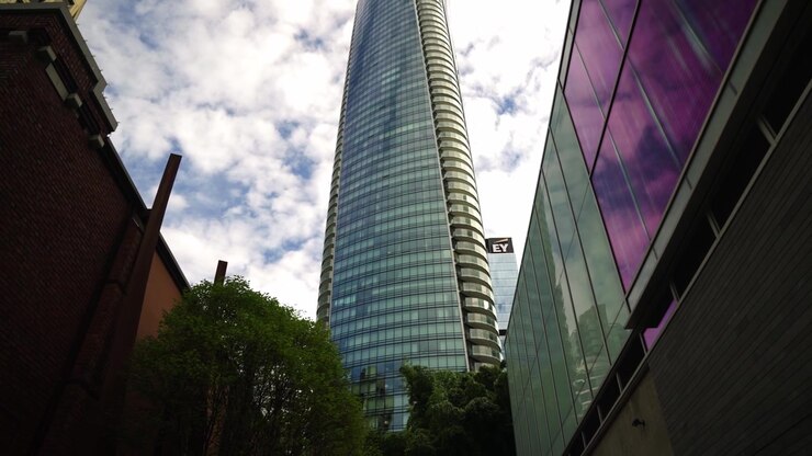 Lento y amplio seguimiento de un moderno y singular edificio de oficinas tipo rascacielos en el centro de Vancouver, cubierto con ventanas de cristal azul de suelo a techo, grabado desde un pequeño callejón con árboles en primer plano
