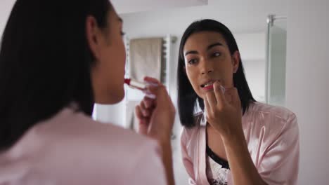 Mixed-race-gender-fluid-person-standing-in-bathroom-and-using-a-lipstick