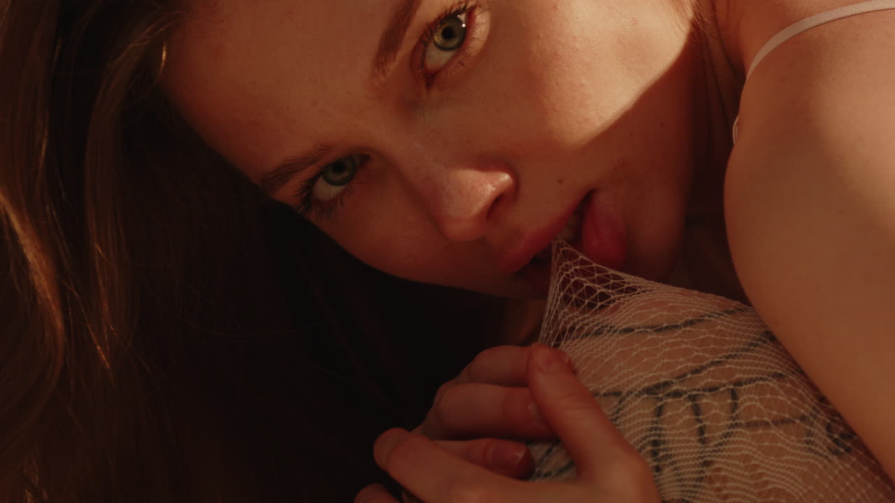 Stunning close up of an enticing woman sensually biting her white stockings while wearing sensual lingerie in slow motion