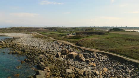 Drone-flight-over-rocky-beach-and-scrubland-foreshore-showing-beach-path-and-heading-inland