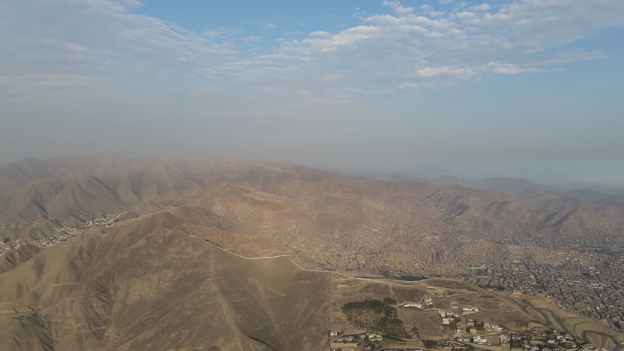 Ripresa aerea di case di Lima su montagne polverose sotto un cielo blu nuvoloso, Perù.