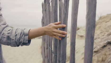 mujer joven mano tocando los sitcks de una pared de madera en la playa, playa nublada