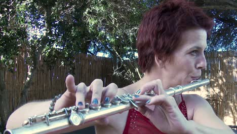 a woman in a red dress plays a tune on a flute outdoors, close up