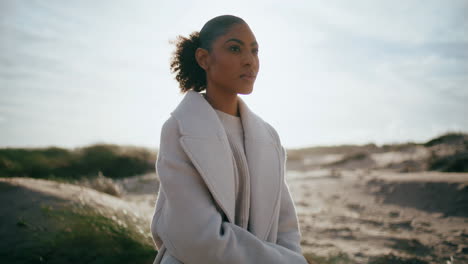 pensive woman resting beach on sunlight. serious african american at sand dunes