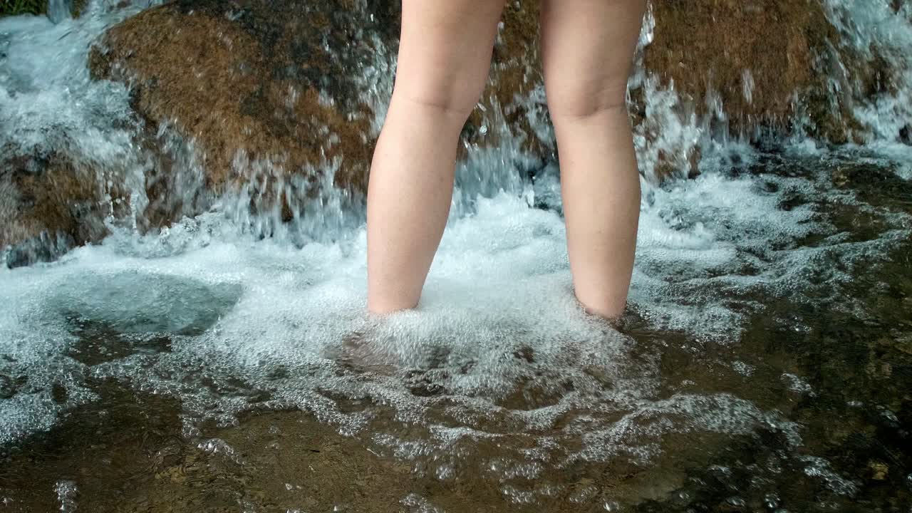 다리를 사용하여 자연 폭포에 몸을 담그는 여성