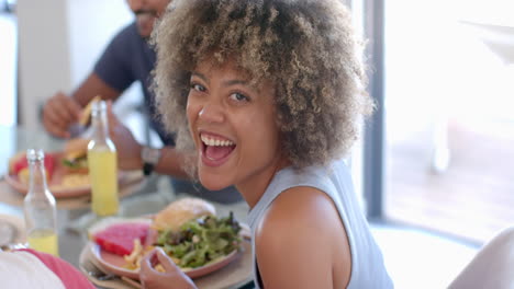 smiling woman enjoying meal with diverse friends, eating salad and sandwich at table