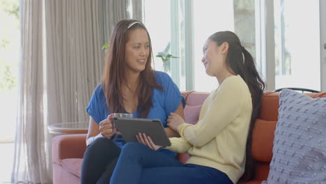 sitting on couch, asian mother and daughter using tablet and smiling together