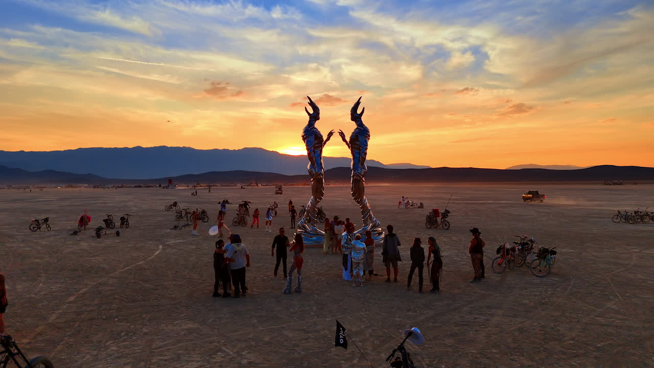 Nevada, USA, 14 August 2025: Sunset Gathering Around Sculptures at Burning Man. Participants gather near tall sculptures in the warm sunset glow on the open playa