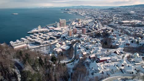 aerial view of trondheim town, norway on cold winter morning, snow capped buildings, homes, fjord and street traffic