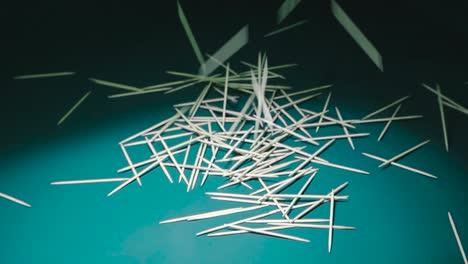 yellow and brown wooden toothpicks being thrown on a dark green background with good lightning and shadows in slow motion creating a pile of toothpicks and casting shadows in 4k resolution