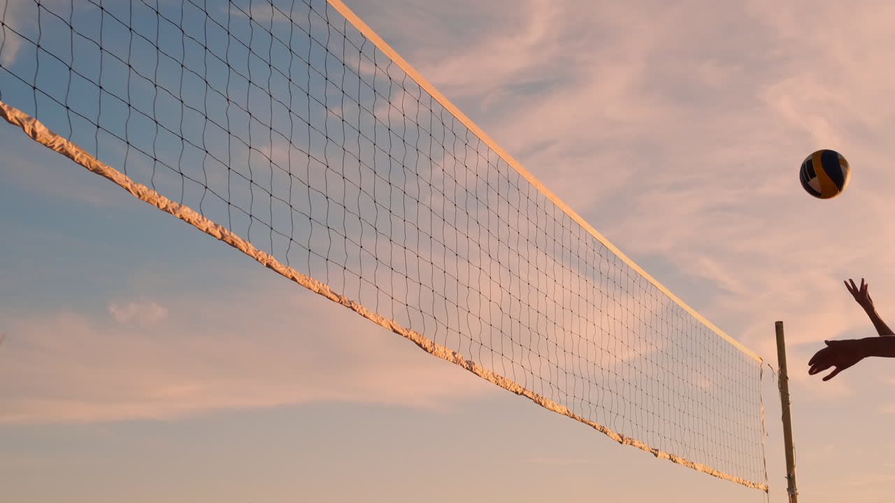 Athletic girl playing beach volleyball jumps in the air and strikes the ball over the net on a beautiful summer evening. Caucasian woman score a point.