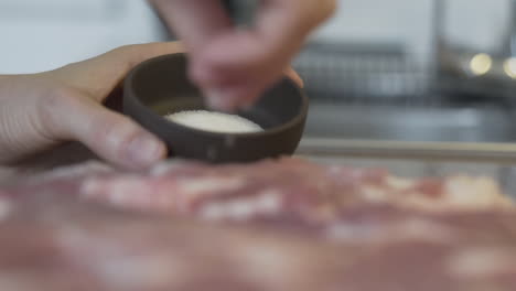 selective focus blurry shot as taking out salt and seasoning raw meat with it in the kitchen, preparing food