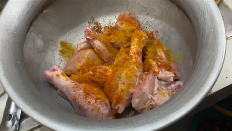 slow dolly out from raw chicken leg pieces sprinkled with spice in metal bowl in kitchen