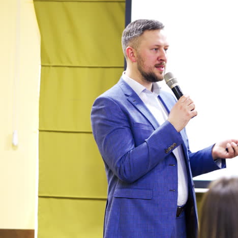 speaker man in blue suit at the stage talking to the microphone at business conference. executive leader speaks and gesticulates at public seminar.