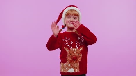 Girl-in-Christmas-sweater-waves-hand-palm-in-hello-gesture-welcomes-someone-to-celebrate-New-Year