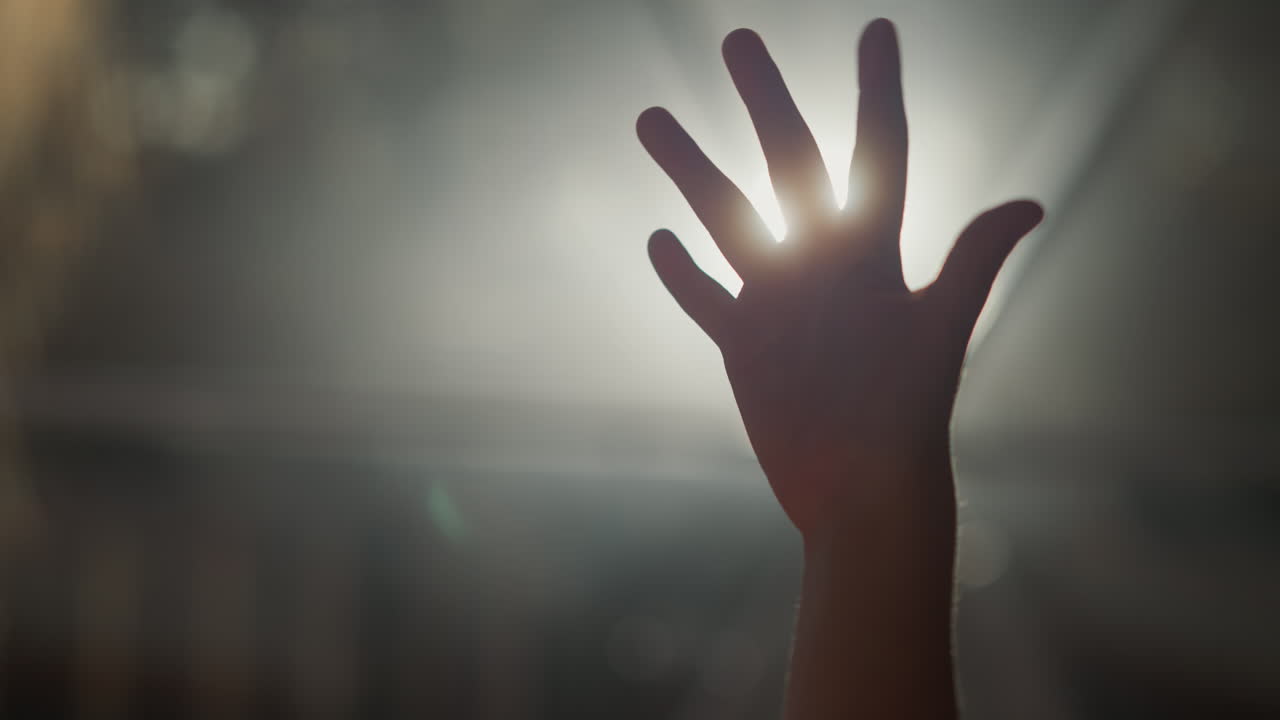 Child hand silhouette at backlight. Little kid bends fingers holding palm against glowing lamp in dark room. Child plays with light beams closeup