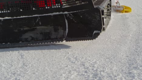 close up of a snow groomer passing by, starting at front with shovel, tracked tires and roller in back, creating fresh new slope with corduroy pattern, slow motion