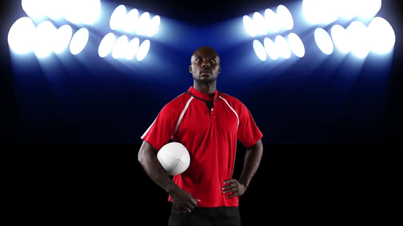 Professional rugby player holding a ball in front of stadium spotlights