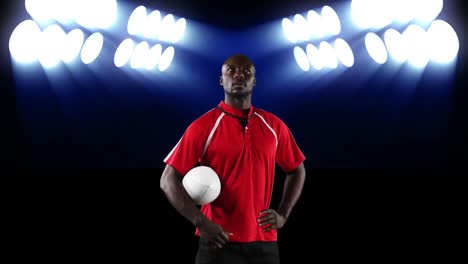 professional rugby player holding a ball in front of stadium spotlights