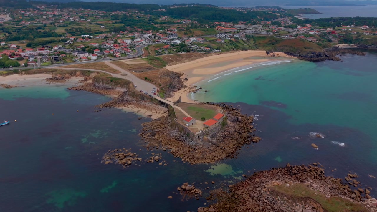 Luftfoto med drone af Nossa Senhora da Lanzada kapellets forbjerg med klippefremspring, turkist vand og den lange A Lanzada strand i Galicien, Spanien.