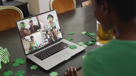 Smiling-diverse-group-of-friends-with-beer-wearing-clover-shape-items-on-video-call-on-laptop