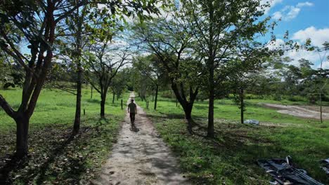 back view of man walking on dirt trail in countryside on sunny day, brazil. aerial