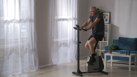 Entrenamiento-De-Salud-En-Bicicleta-Estacionaria,-Un-Hombre-De-Mediana-Edad-Está-Girando-Pedales,-Ejercicio-Para-La-Respiración-Y-El-Sistema-Cardiovascular,-Atención-Médica-Y-Deporte