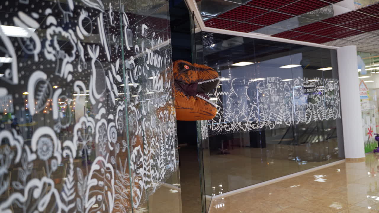 Orange dinosaur peeping from behind the shop window decorated with ornaments. Sneaky T-Rex running by the shopping mall.