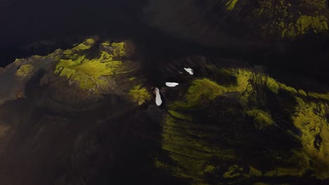 Aerial-view-over-natural-textures-and-patterns-of-the-Icelandic-highlands-dark-mountain-terrain,-covered-in-bright-green-grass