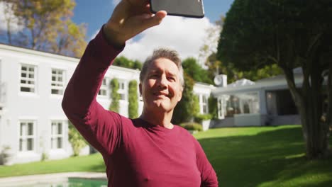 Feliz-Hombre-Caucásico-Mayor-Tomando-Selfie-Con-Un-Teléfono-Inteligente-De-Pie-En-El-Jardín-Sonriendo